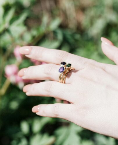 Close-up of a woman's hand adorned with gemstone rings, showcasing luxury and elegance against a natural backdrop.